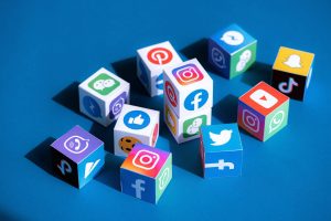 Cubes colorés représentant divers logos de plateformes de médias sociaux, dont Facebook, Twitter, Instagram, Snapchat et TikTok, disposés sur une surface bleue.