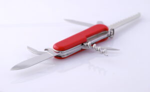 Un couteau suisse rouge doté de multiples outils, dont une lame, un ouvre-boîte, un tire-bouchon et une scie, est élégamment présenté sur une surface réfléchissante. Idéal pour les passionnés d'aventure ou comme cadeau classique, inspiré du cœur du e-commerce suisse.