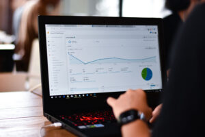 Une personne examinant un tableau de bord d’analyse, rempli de graphiques et de tableaux sur un écran d’ordinateur portable dans un environnement intérieur lumineux, cherche à remédier au problème de son site n’apparaît pas sur Google grâce à des stratégies de référencement efficaces.